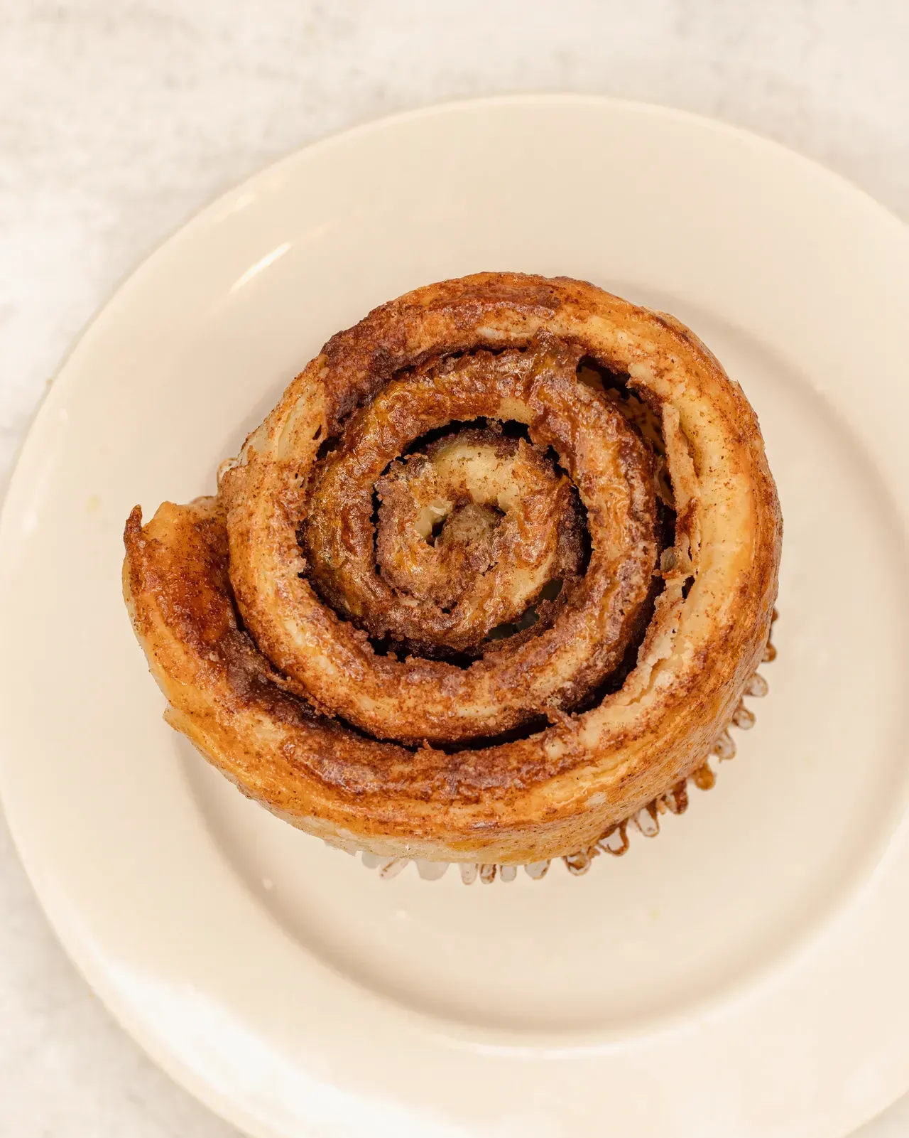 Cinnamon roll in a paper cup on a white plate.