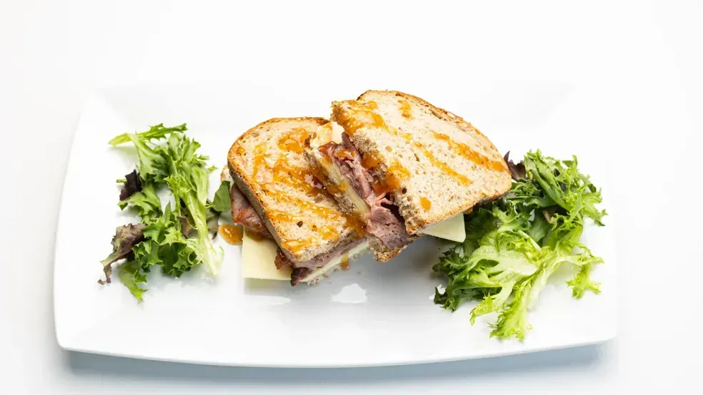 Grilled sandwich cut in half on a white plate with greens on a white background.