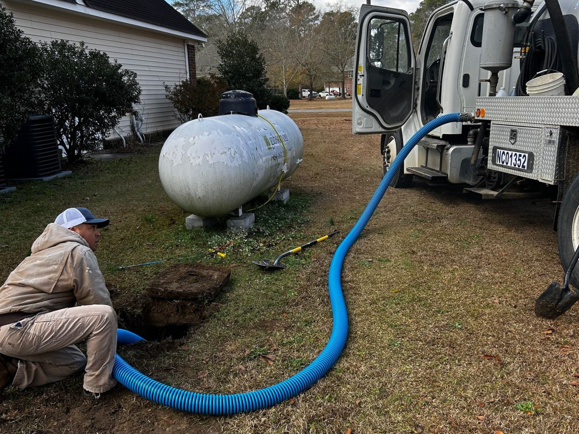 Person connects blue hose to a propane tank next to a white truck on a lawn.