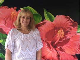 A woman is standing in front of a painting of red flowers.