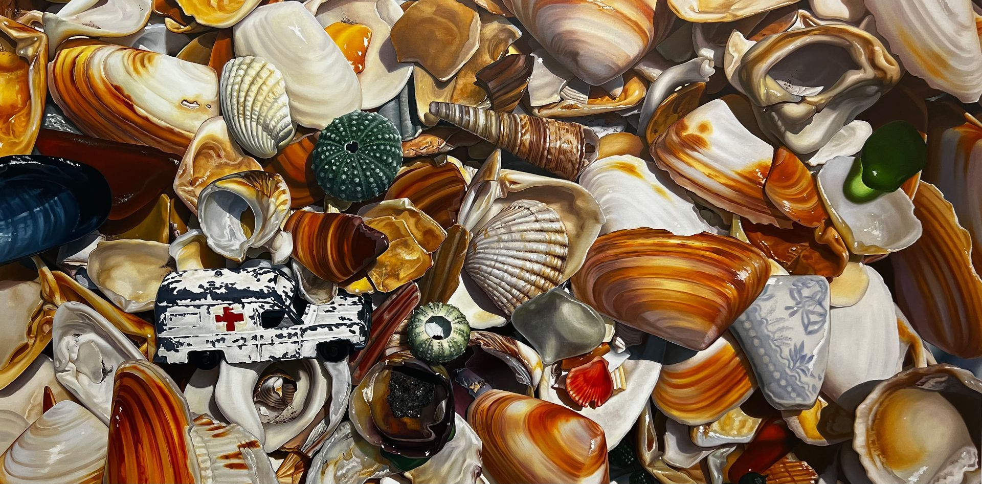 A collection of mixed seashells, with a small, white toy ambulance resting among them.