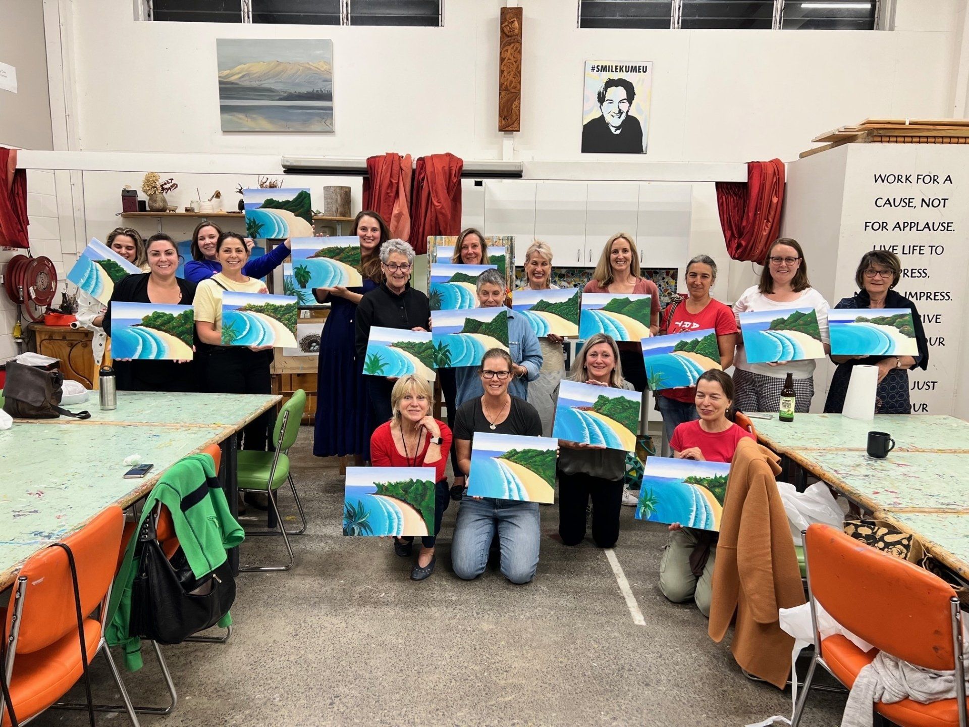 A group of people are posing for a picture in a room holding paintings.