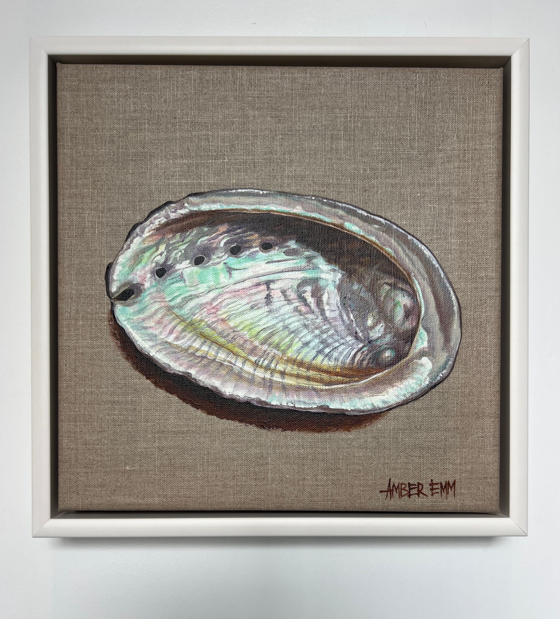 A painting of an iridescent abalone shell set against a textured, light-brown linen background in a white frame.