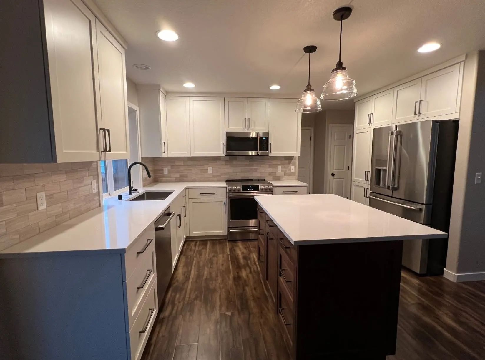 Modern white kitchen with stainless steel appliances, dark island, and recessed lighting