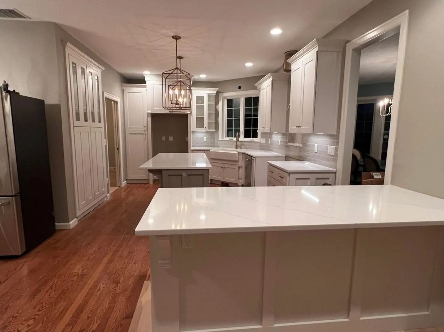 Bright modern kitchen with white cabinets, large island, hardwood floors, and recessed lighting