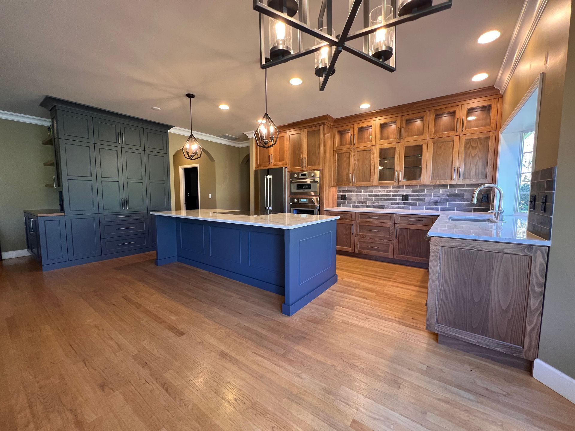 A modern kitchen with white upper cabinets, a grey island, stainless steel appliances, and under-cabinet lighting.