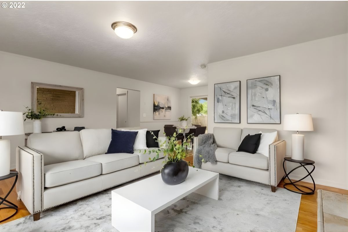A living room with two light-colored sofas, a white coffee table, a grey area rug, and wall art on a neutral wall.