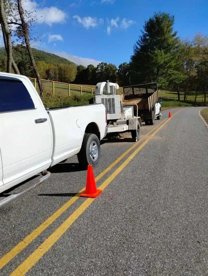 White pickup towing a trailer on a rural road, with an orange traffic cone behind it.