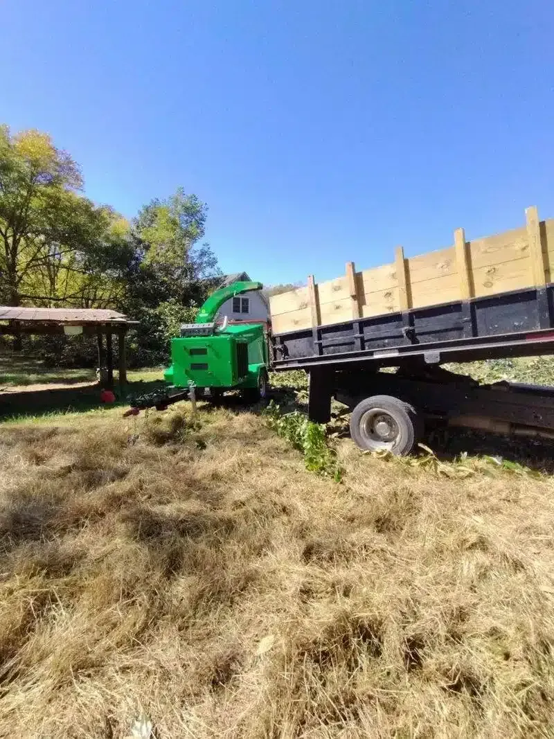 Green truck with a flatbed trailer in a grassy field under a clear blue sky