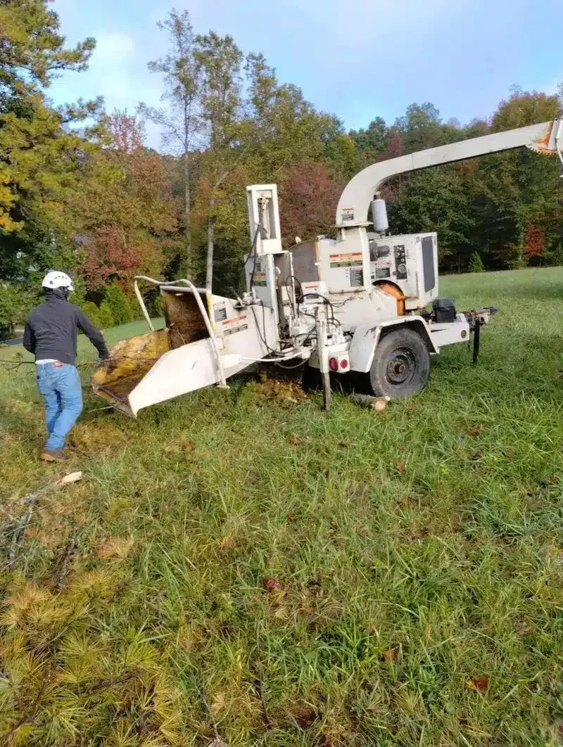 White wood chipper in grassy field with a person standing beside it and trees in the background