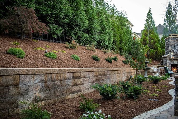 A stone wall surrounds a lush green hillside in a backyard.