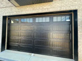 Black paneled garage door set in a light brick wall with a concrete driveway foreground