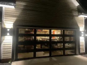 Lit storefront with large glass garage door at night, white siding and exterior lights
