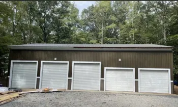 Five white garage doors on a brown storage building in a wooded lot