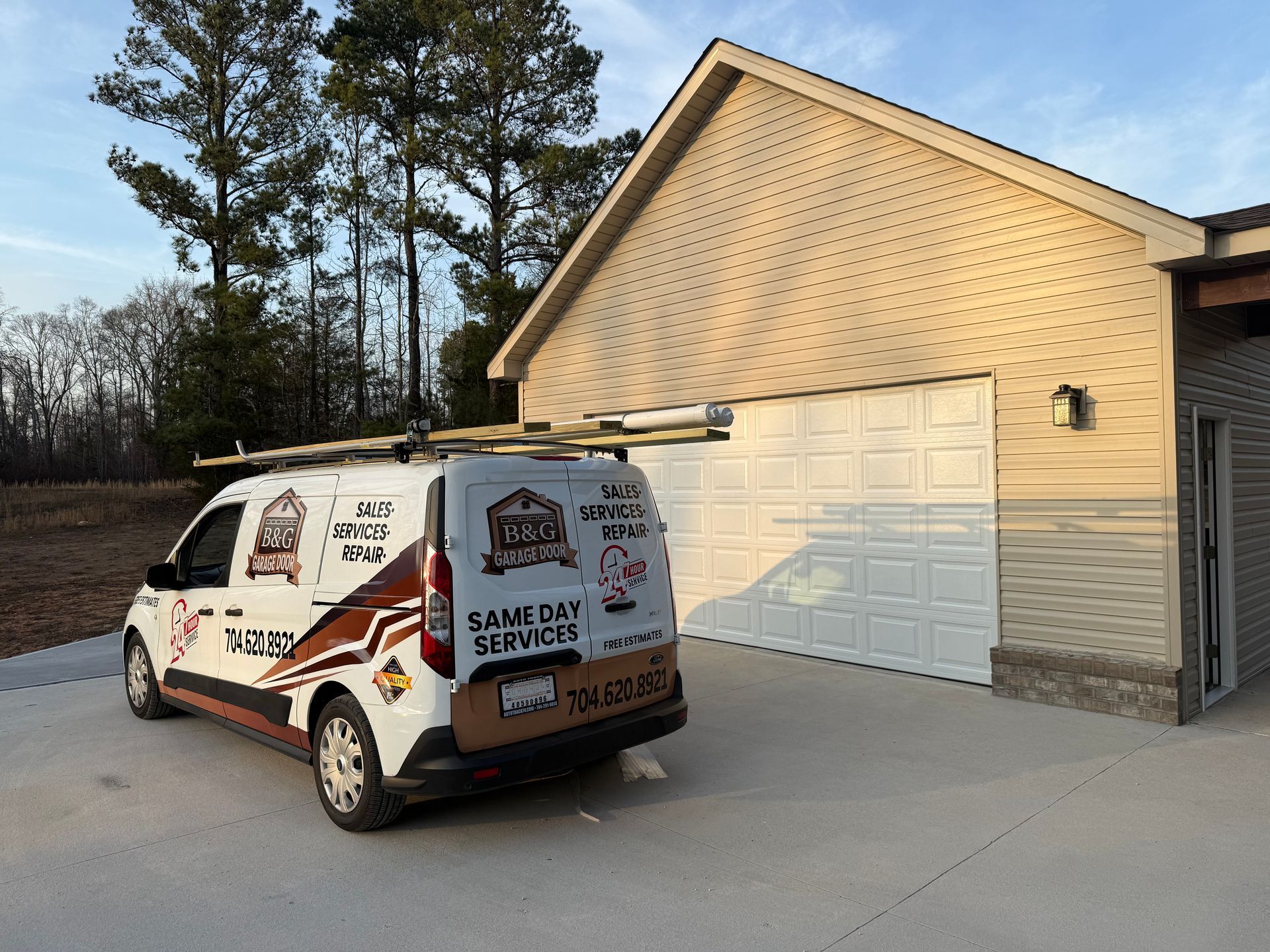 White service van parked beside a beige garage on a driveway, with trees in the background.