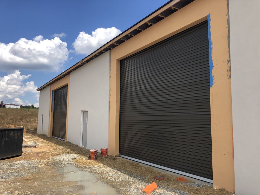 Row of unfinished buildings with closed metal garage doors under a cloudy sky