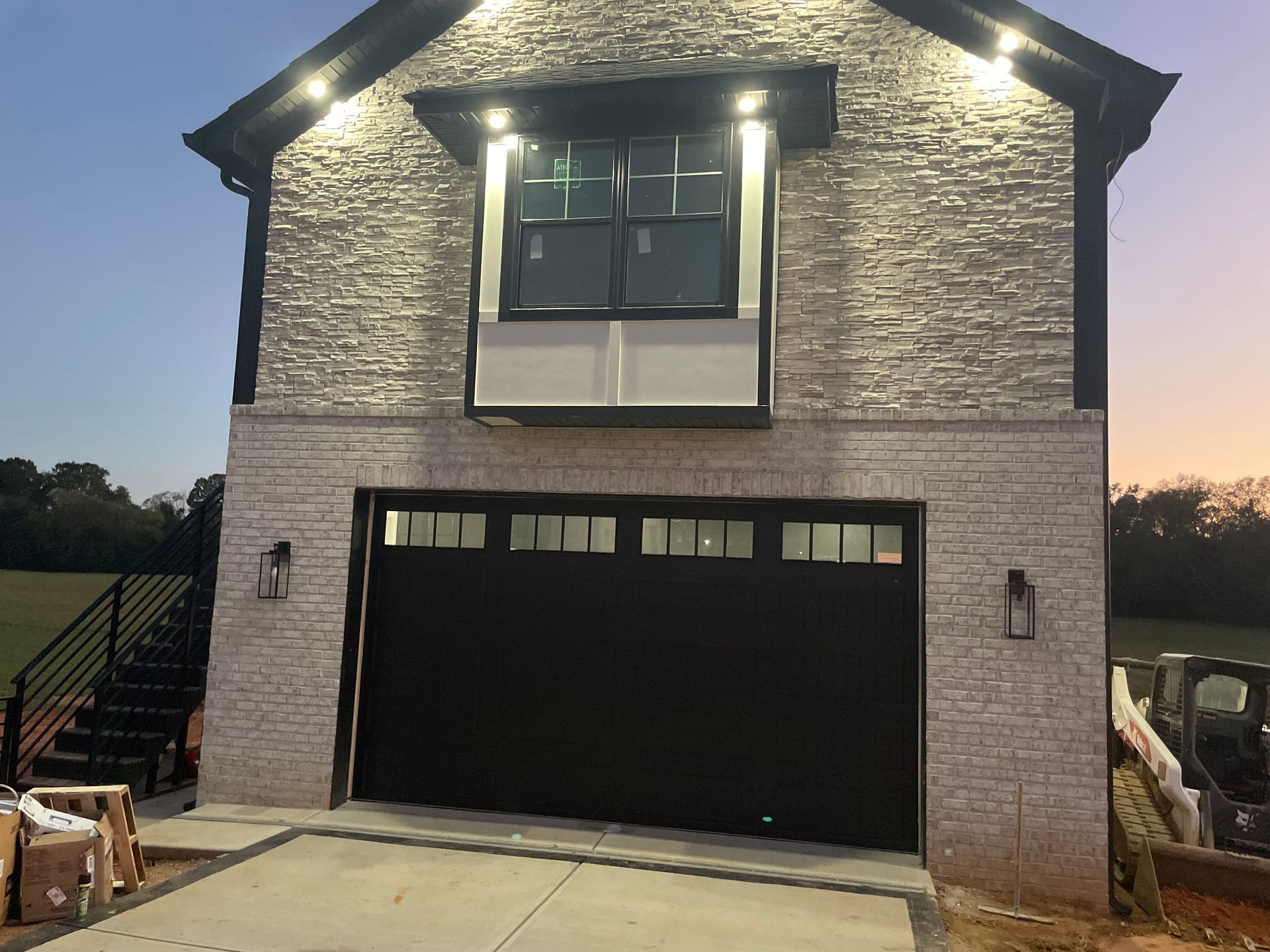 New brick house exterior at dusk with lit upper windows and a black garage door
