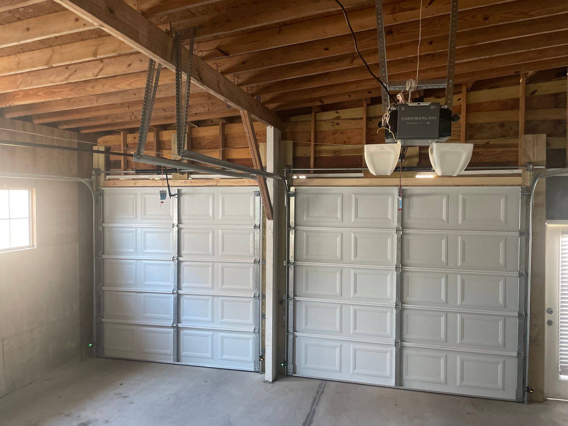 Interior of a garage with two closed white sectional doors and exposed wooden rafters