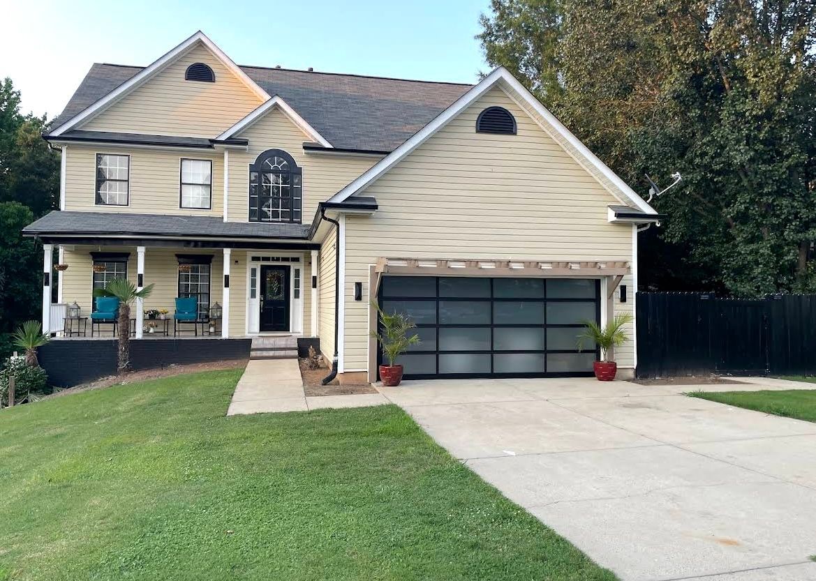 Two-story beige house with a front porch, double garage, and driveway on a green lawn