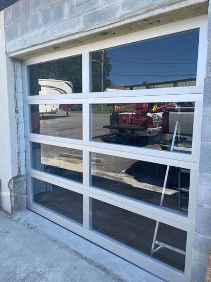 Garage door with white window panels reflecting a red tractor outside.