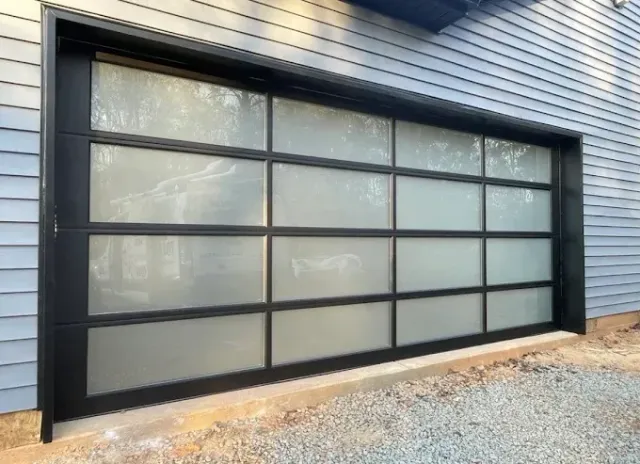 Large frosted glass garage door with black trim on a blue-sided house exterior