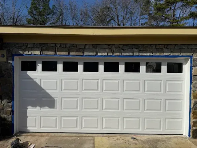 White garage door with small windows under a roof, framed by stone walls.