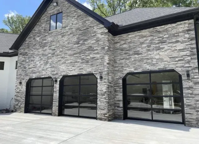 Stone-sided house with black-framed glass garage doors and a paved driveway