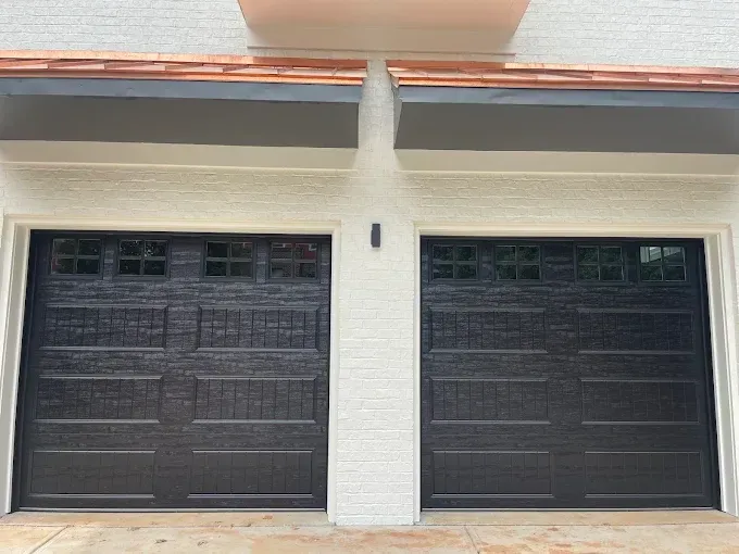 Two black garage doors on a white house exterior under a covered roofline