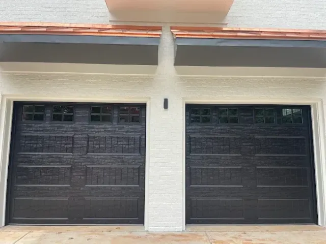 Front view of a white house with two black garage doors and a small upper balcony.
