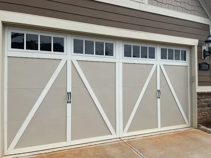 Three beige garage doors with white trim and diagonal braces on a house exterior.