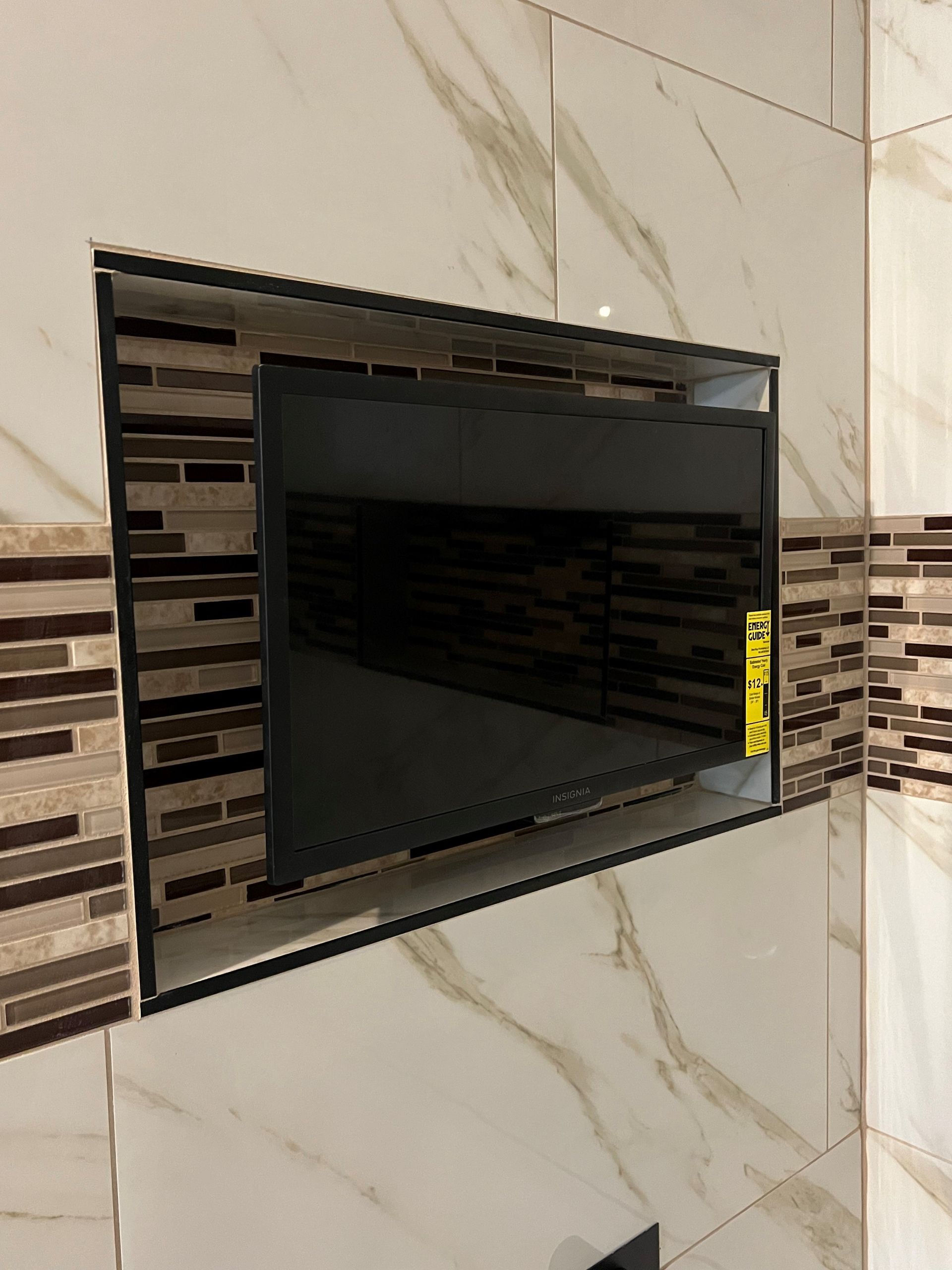 Wall-mounted black TV in a tiled bathroom or kitchen niche with striped accent tiles