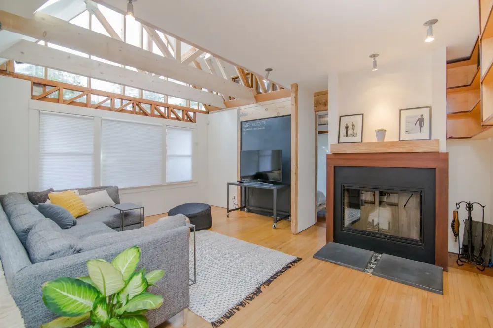 Modern living room with a gray sectional, fireplace, high beamed ceilings, and natural wood flooring