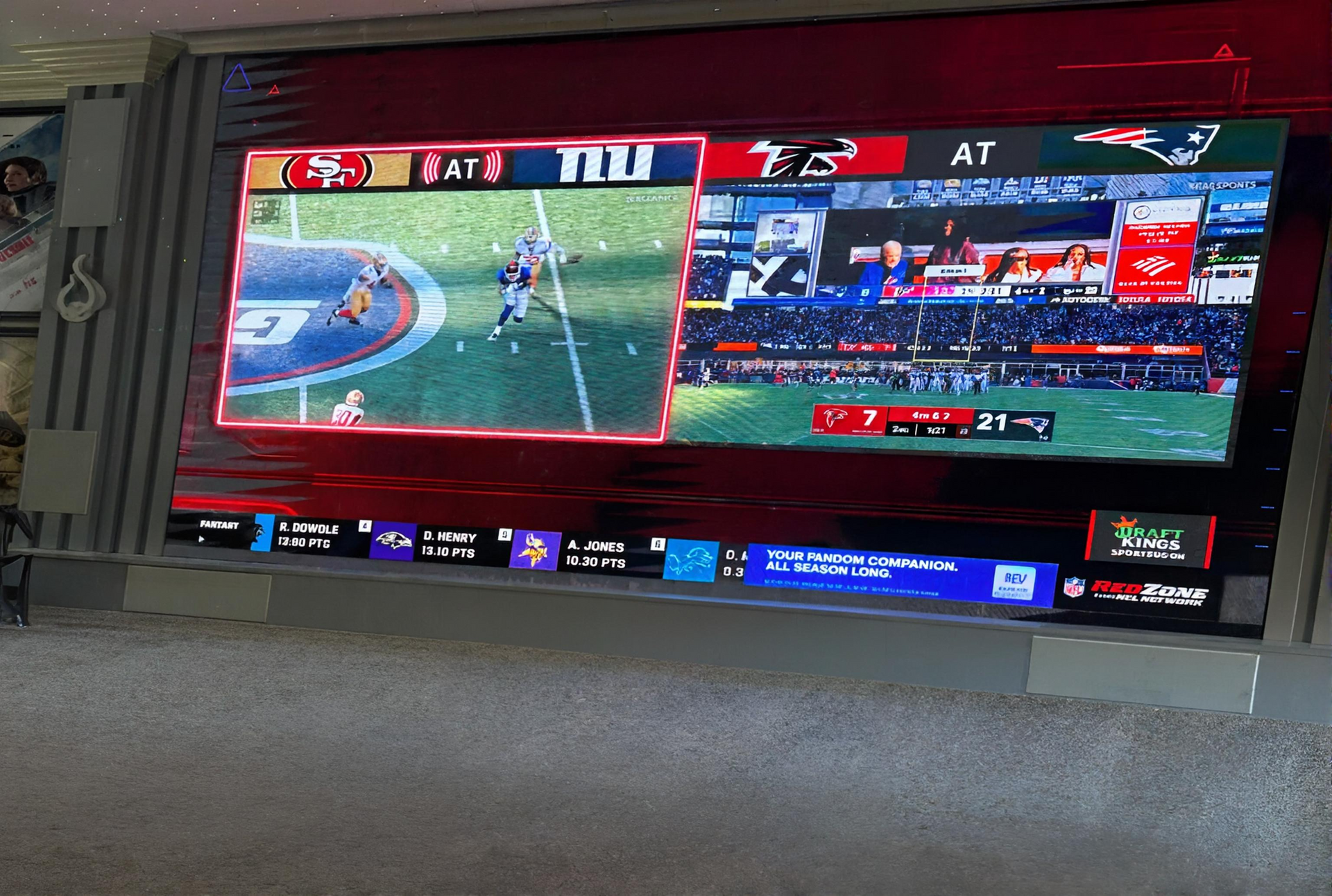 A wide screen displays two football games simultaneously, featuring team logos for the 49ers, Giants, Falcons, and Patriots