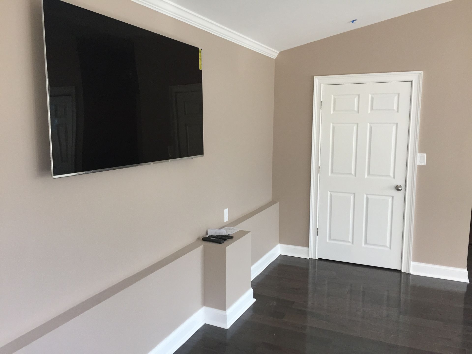 Empty living room with beige walls, dark tile floor, wall-mounted TV, and white door