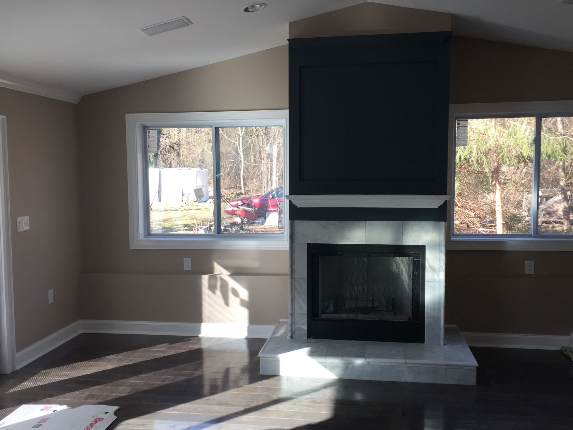 Empty living room with a gray fireplace and large windows letting in sunlight