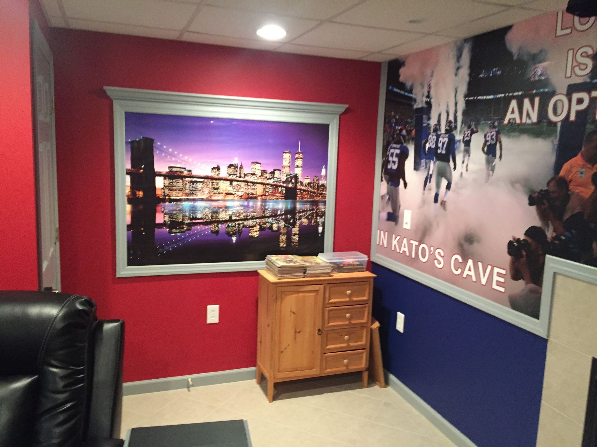 Red and blue lounge with framed city skyline art, black chair, and a small wooden cabinet