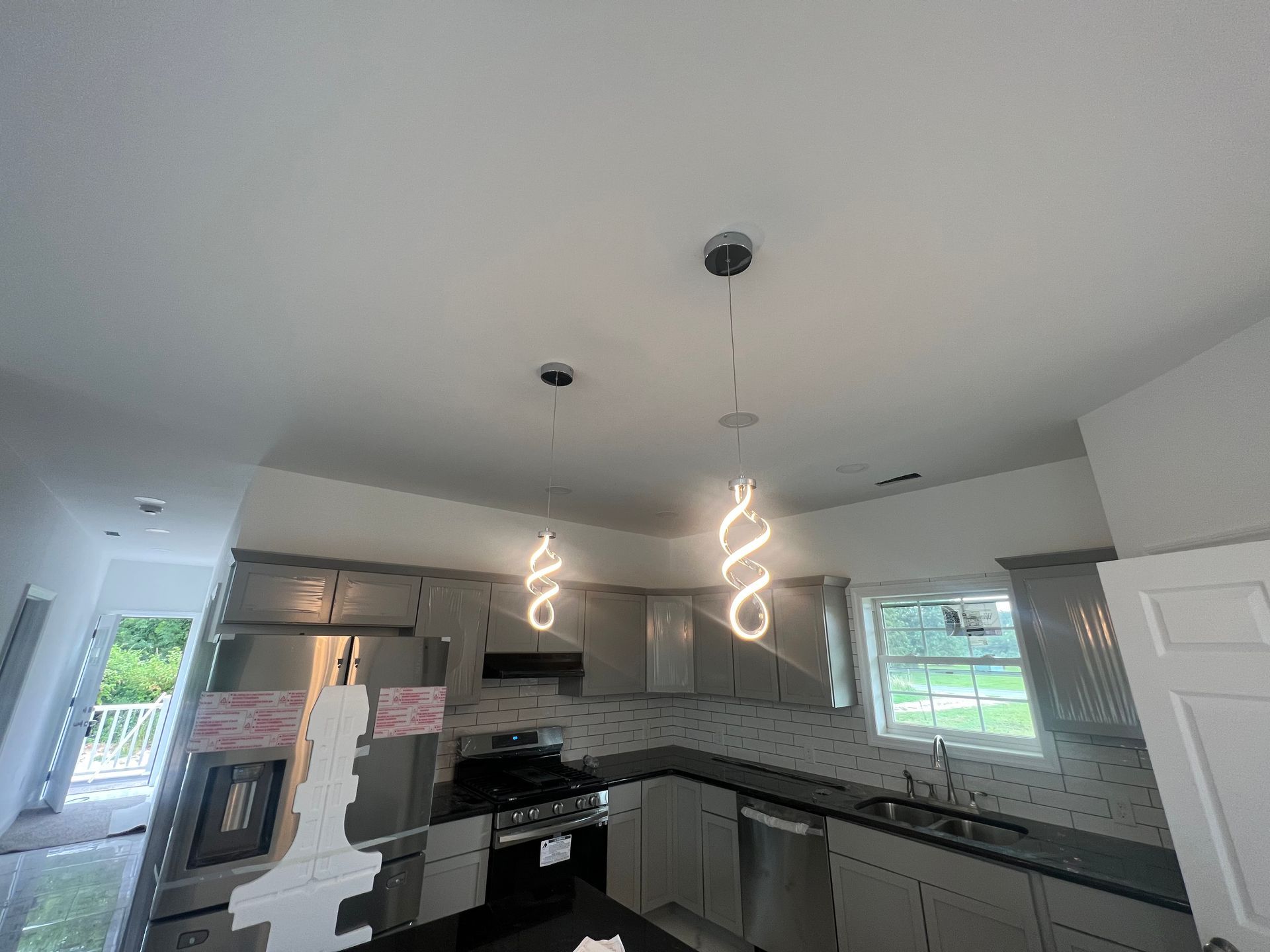 Modern kitchen with white cabinets, gray tile backsplash, black appliances, and pendant lights