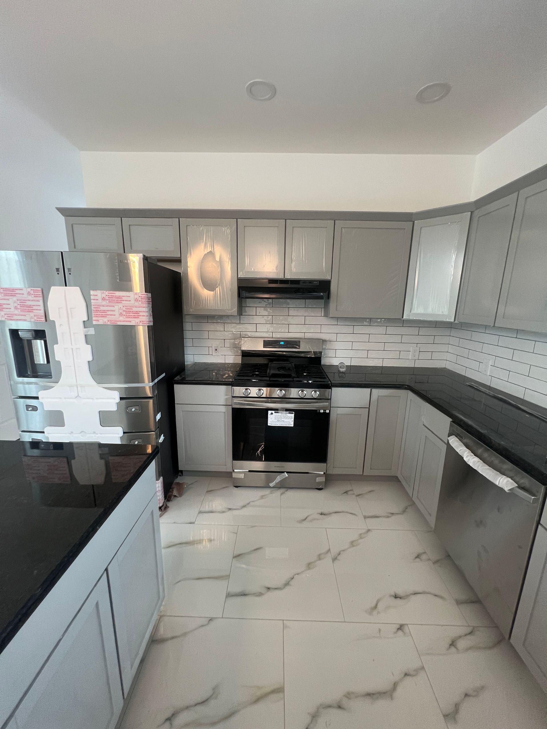 Modern gray kitchen with stainless appliances, black counters, and white marble-style floor tiles