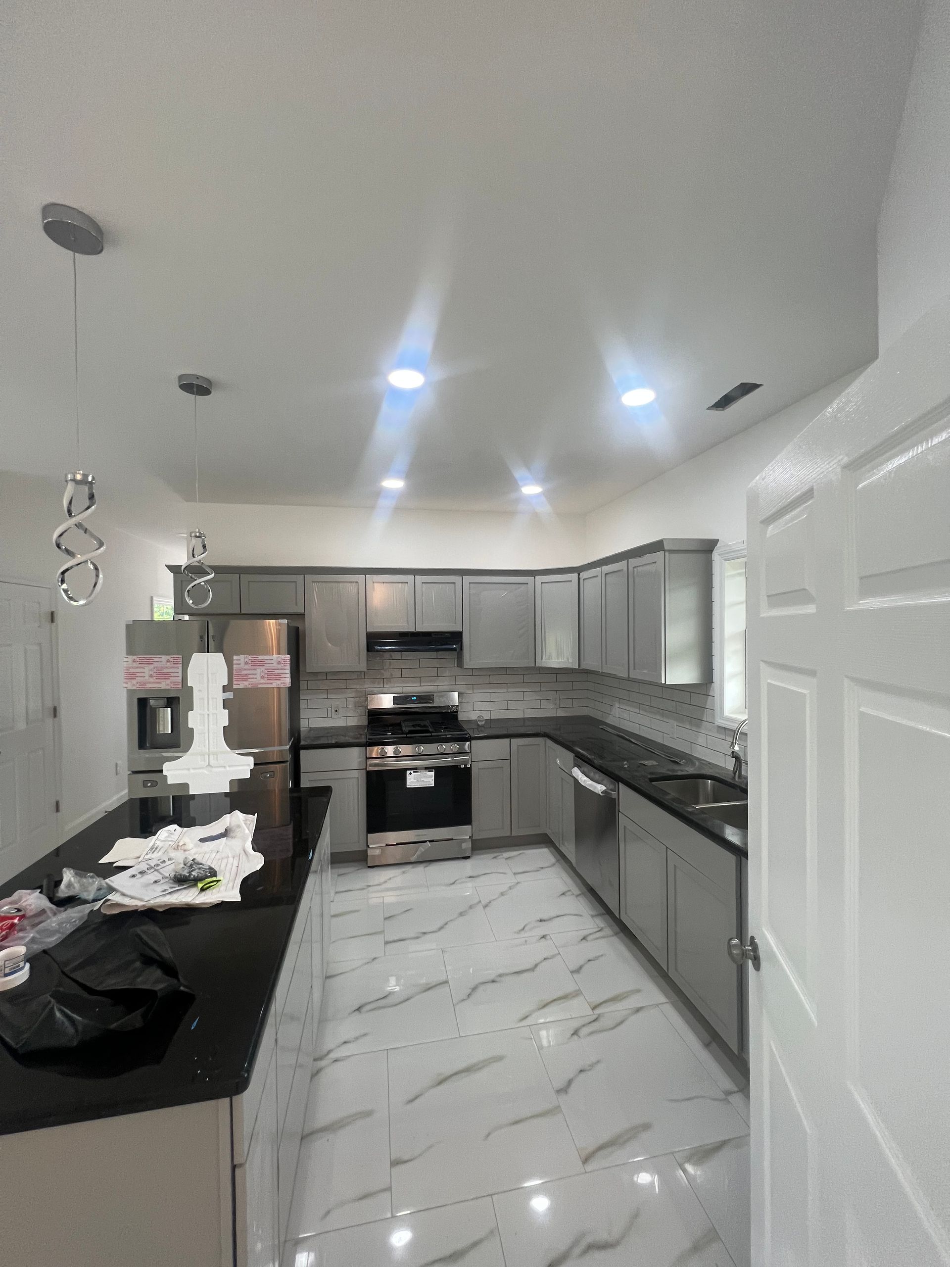 Modern kitchen with gray cabinets, black countertops, marble-look tile floor, and recessed ceiling lights