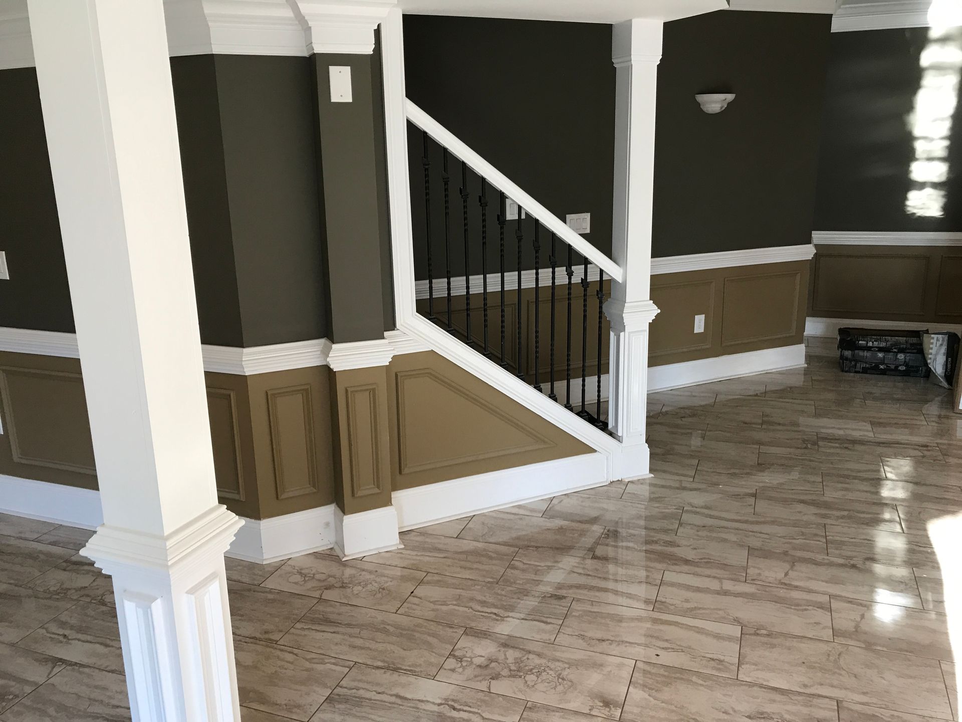 Empty interior foyer with white staircase, brown wainscoting, and glossy tile floor