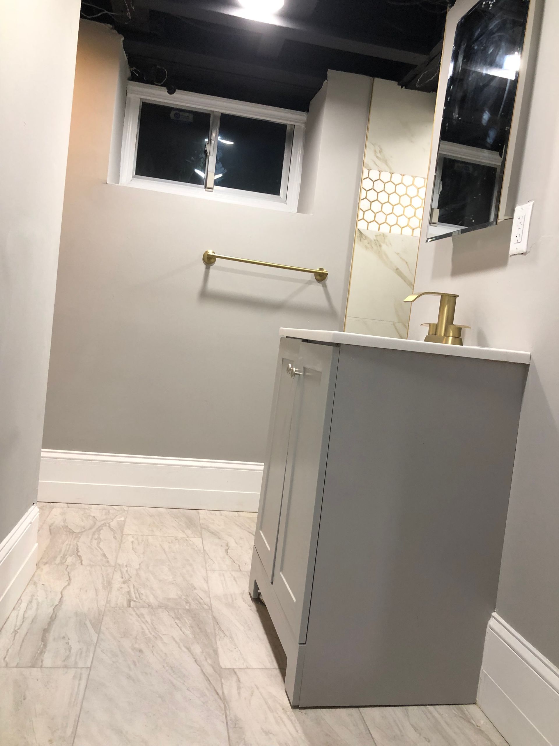 Small bathroom with gray vanity, marble-look floor, white walls, window, towel rack, and mirror cabinet