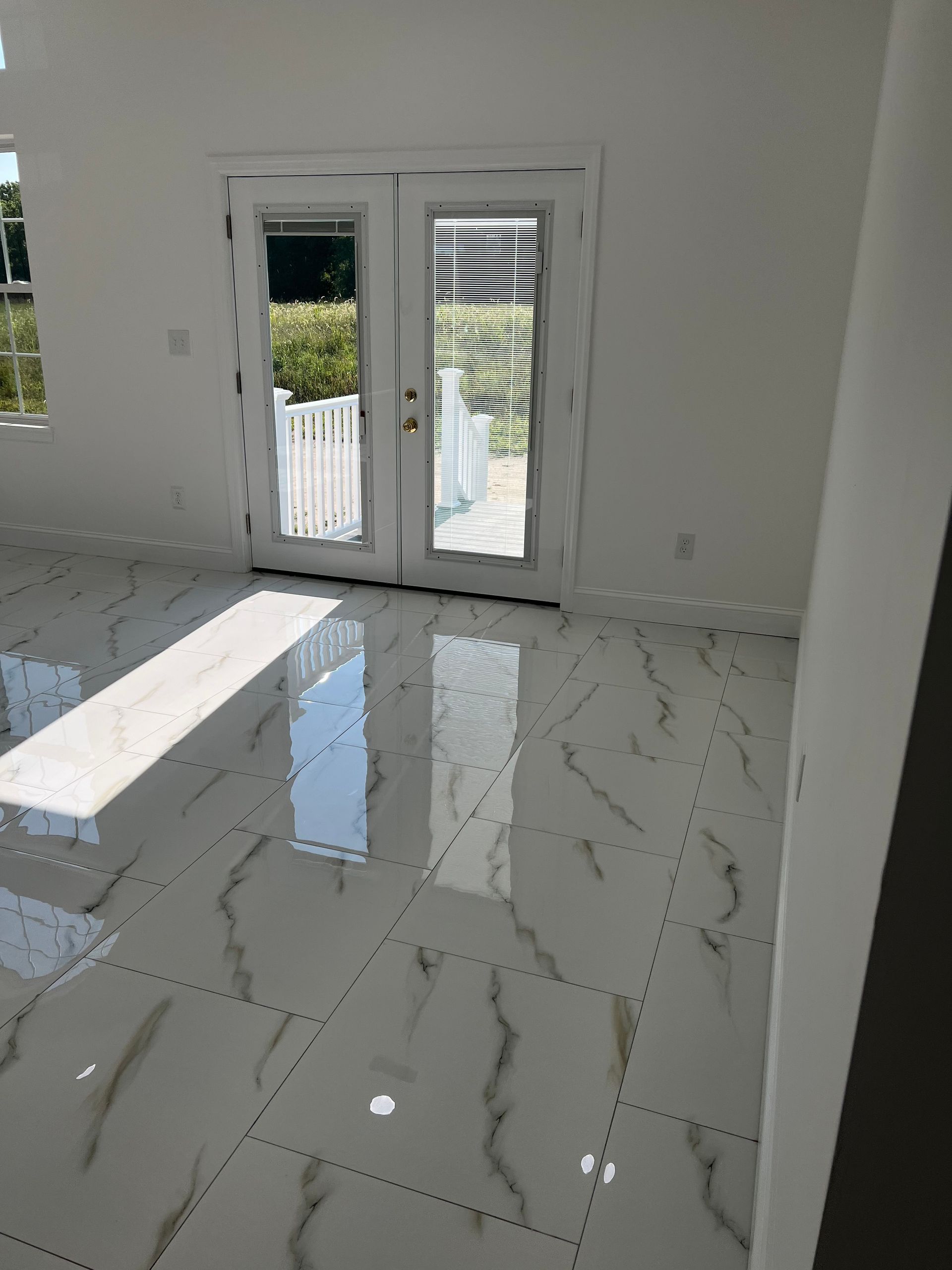 Bright empty room with white marble floor and glass double doors opening to a balcony.