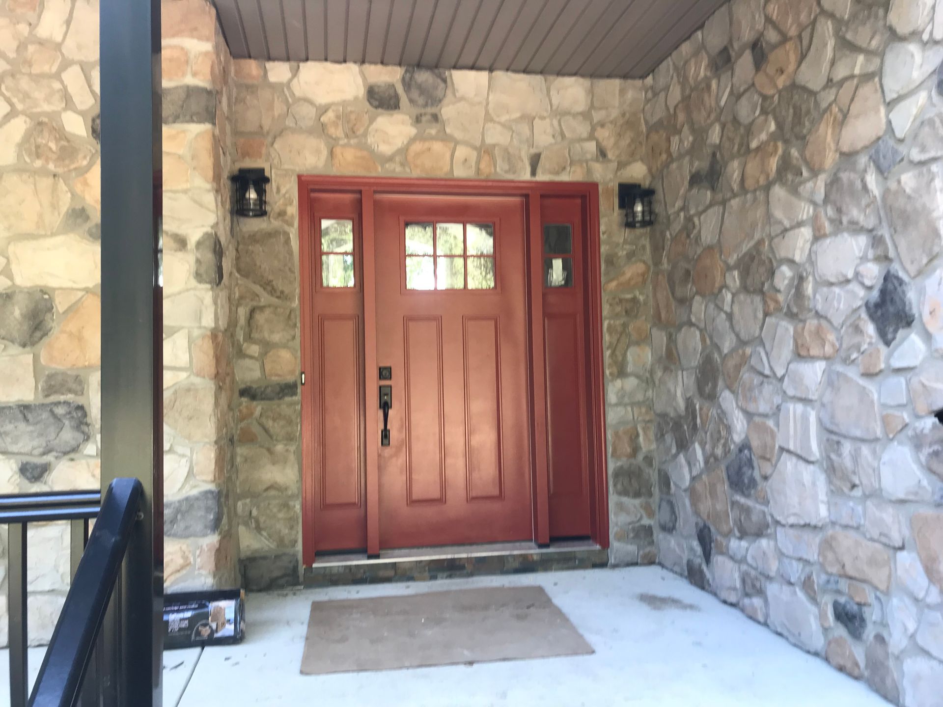 Red front door in a stone entryway with a porch light and doormat