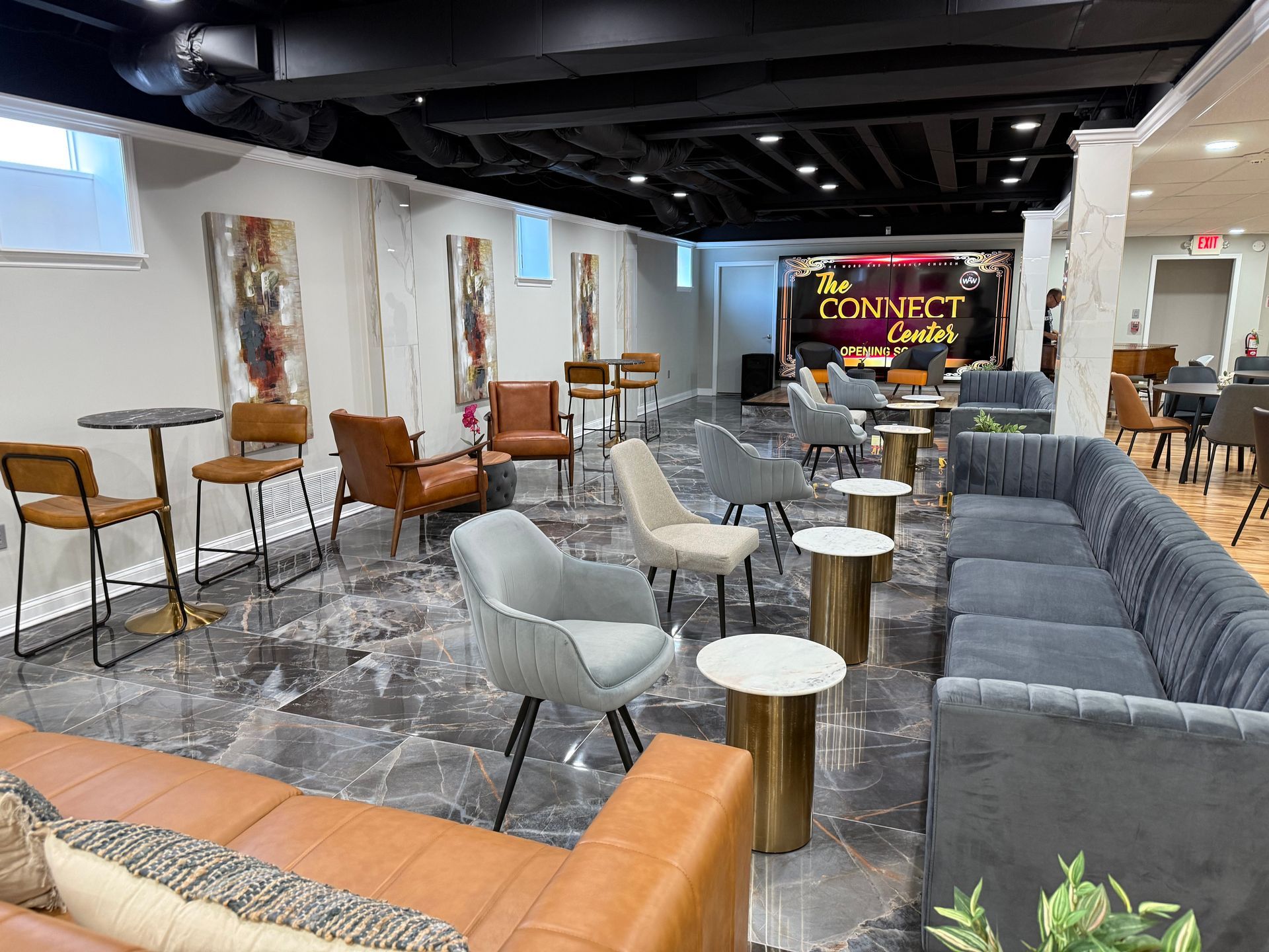 A lounge with modern furniture, leather and fabric chairs, and small gold tables, set on a grey marble floor