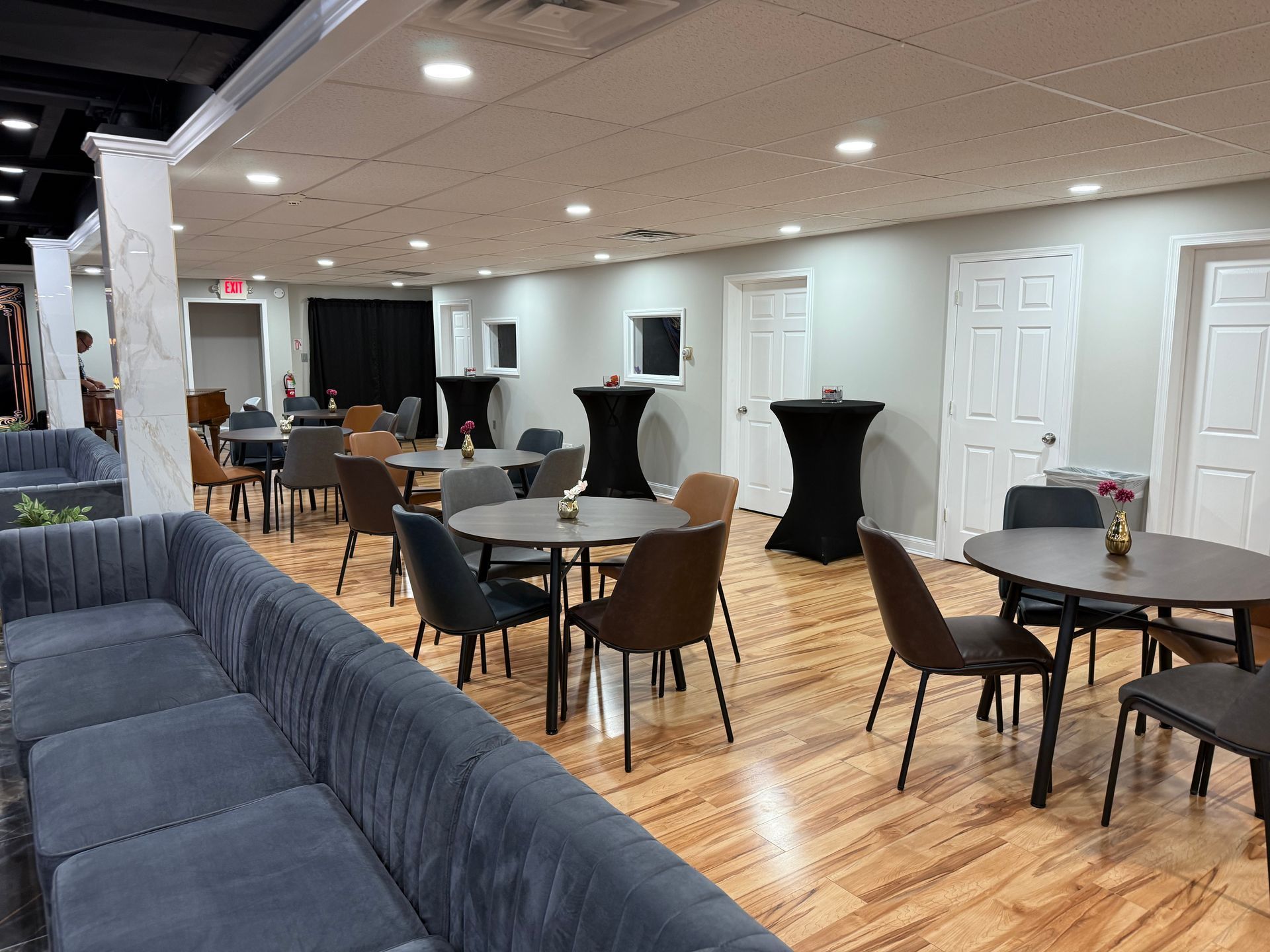 Empty event hall with gray sofas, round tables, wooden chairs, and black cocktail tables on a polished floor