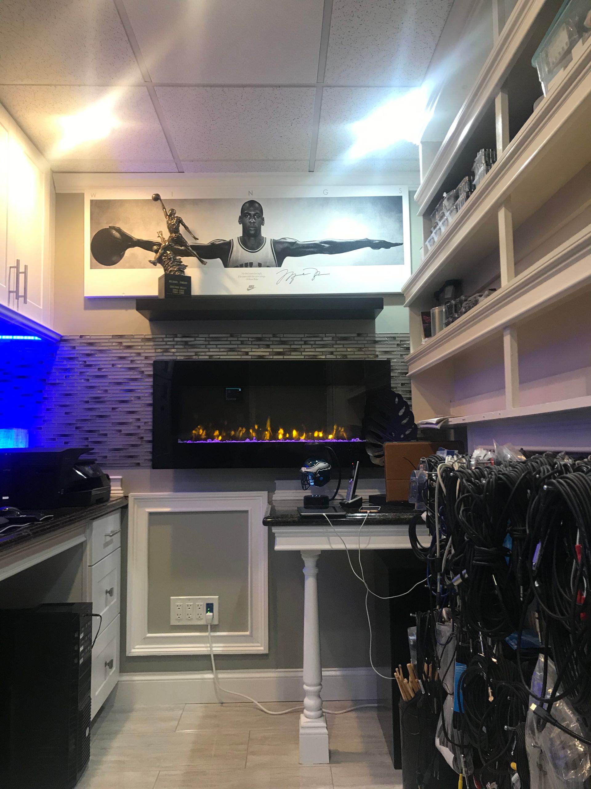 Small room with a lit fireplace, wall shelves, and a desk, viewed from the center aisle