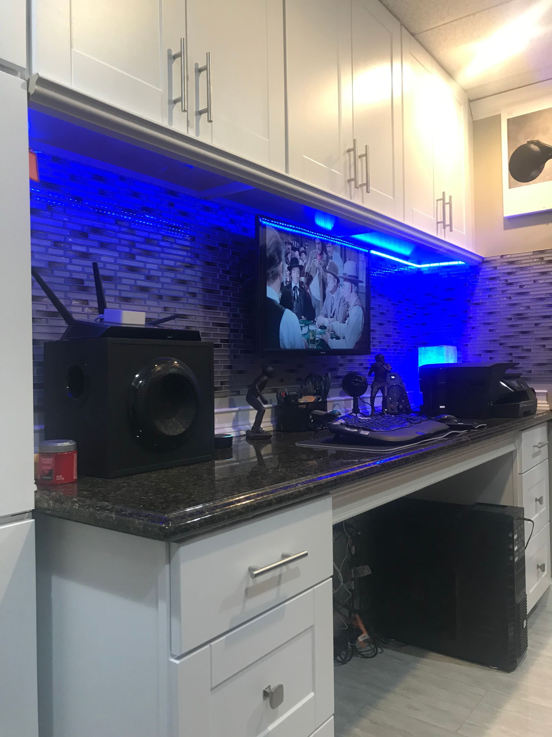 Modern kitchen counter with blue under-cabinet lighting, white cabinets, and black appliances