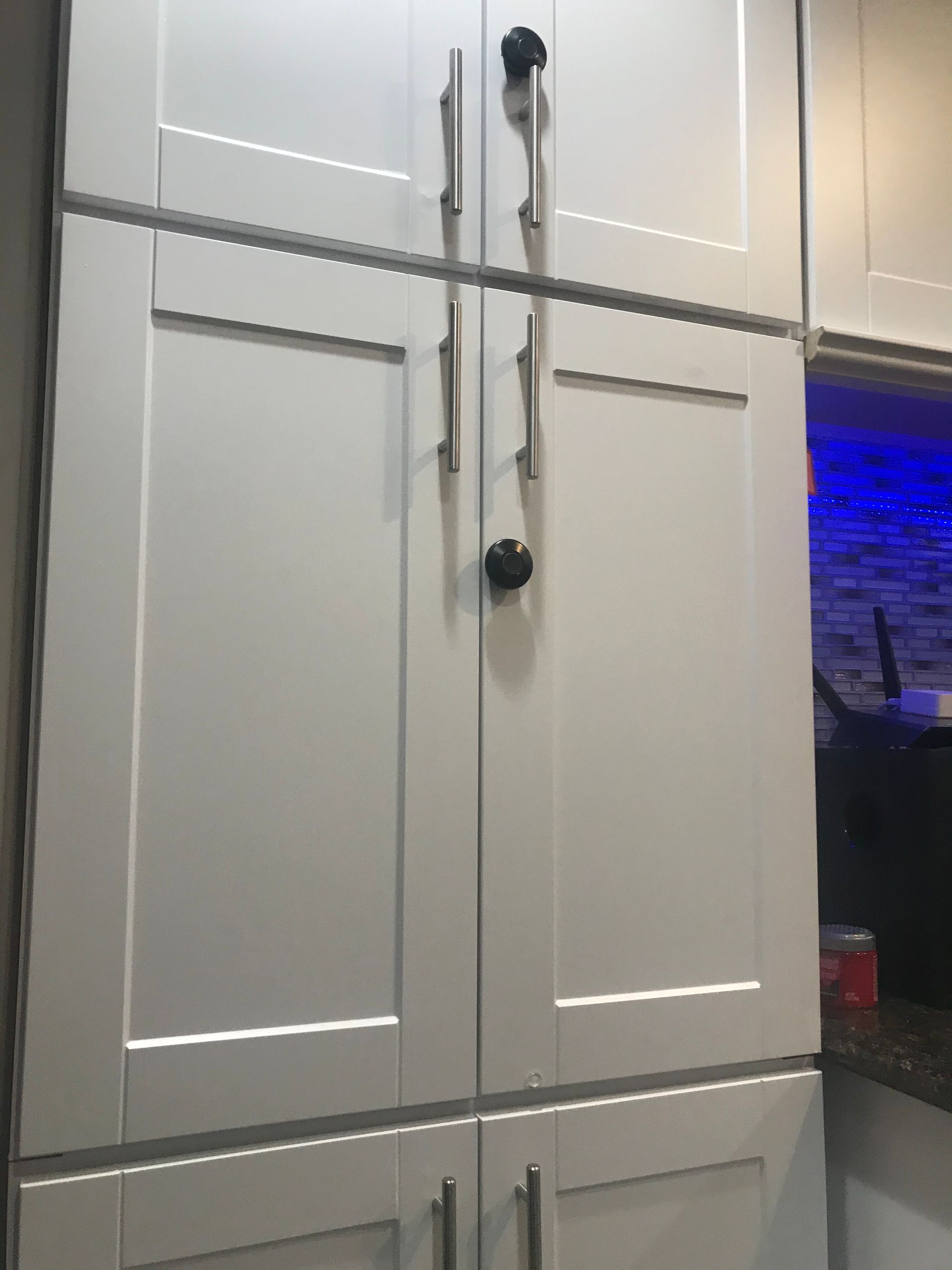 White kitchen cabinets with black handles beside a blue-lit counter area