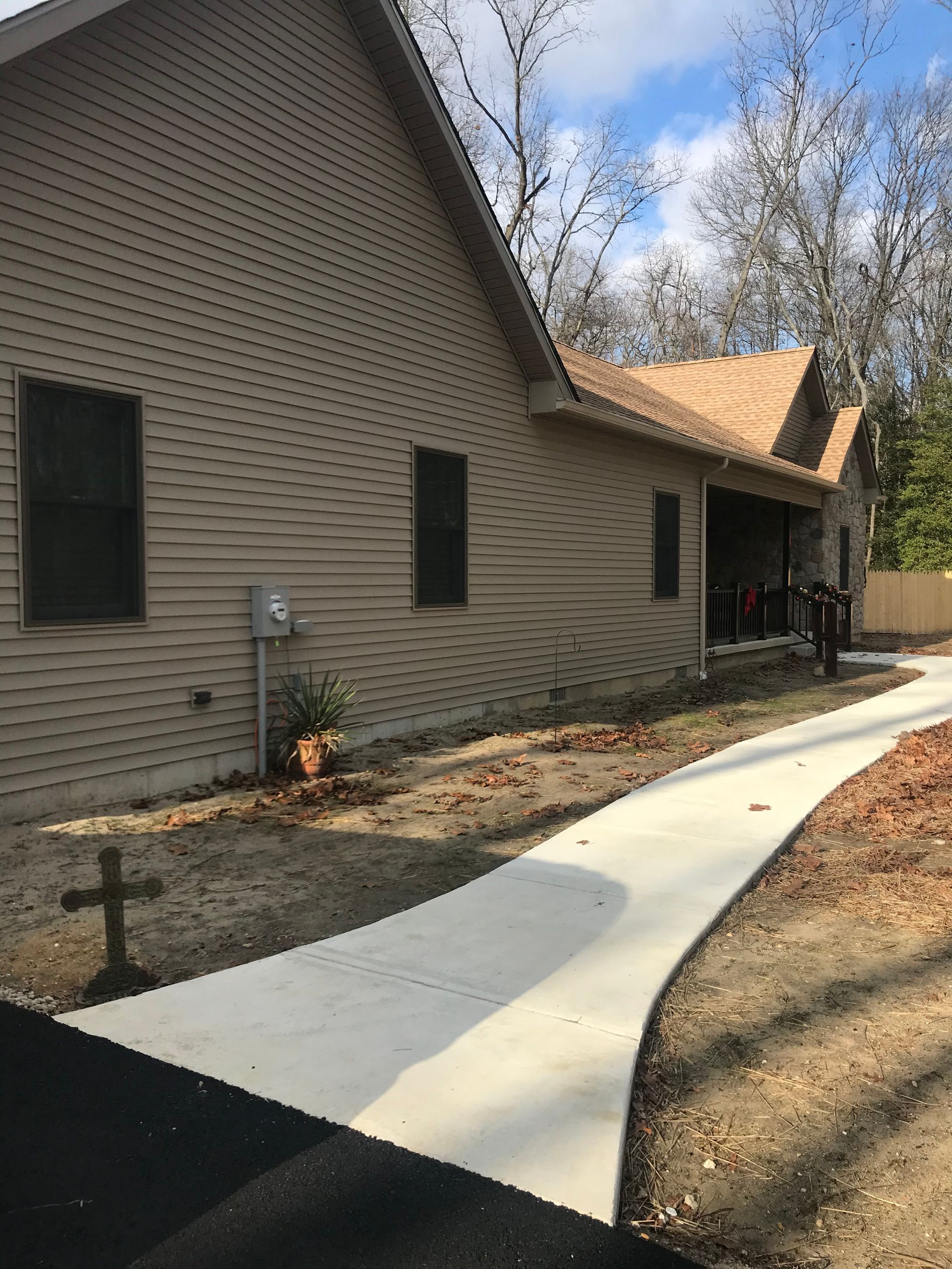 Curved white concrete walkway beside a beige brick house with black windows and winter landscaping