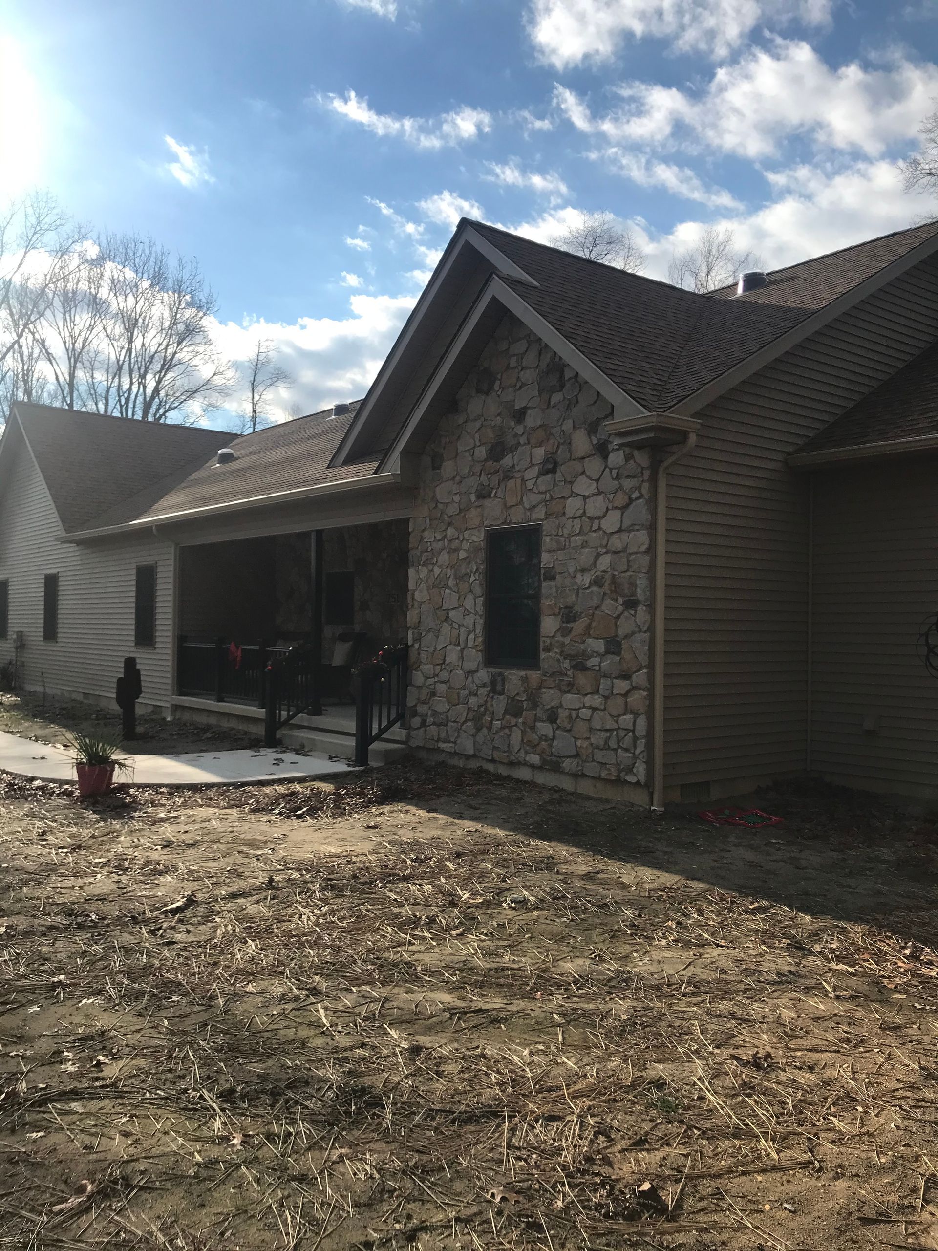 Stone house with a covered front porch and gabled roof in a sunny yard, with trees and blue sky